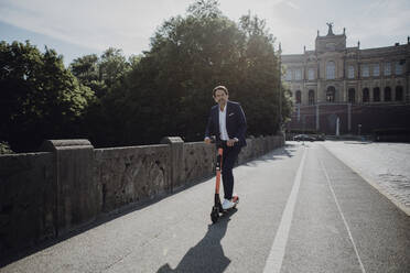 Geschäftsmann mit E-Scooter auf einer Brücke - JLOF00382