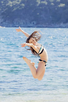 Porträt eines Mädchens, das vor dem Meer in die Luft springt - XCF00285