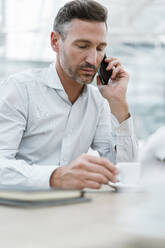 Portrait of businessman in a cafe talking on the phone - DIGF08466