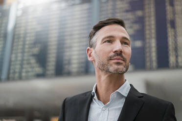 Portrait of businessman at arrival departure board at the airport - DIGF08477