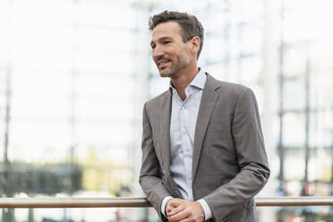 Portrait of smiling businessman leaning against railing - DIGF08479