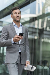 Portrait of businessman with cell phone and newspaper on the go - DIGF08492