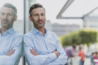 Portrait of a confident businessman leaning against glass front - DIGF08494