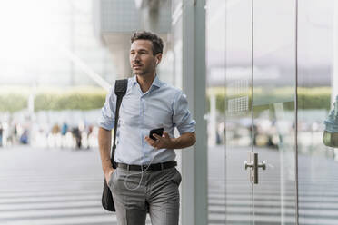 Businessman with cell phone and earphones on the go - DIGF08501