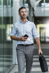 Businessman with cell phone and earphones on the go - DIGF08505