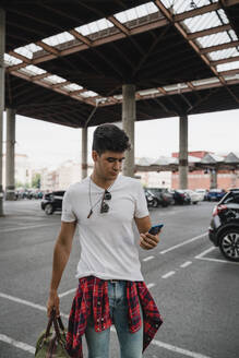 Young man at train station with smartphone - JMHMF00007