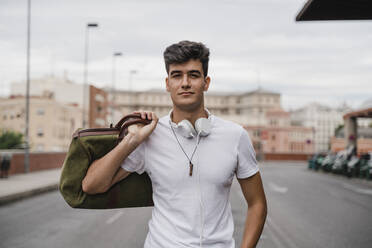 Junger Mann mit einer Tasche am Bahnhof und Kopfhörern - JMHMF00016