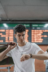 Junger Mann prüft die Uhrzeit am Bahnhof - JMHMF00019