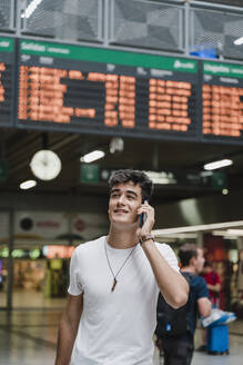 Young man waiting at train station and using smartphone - JMHMF00021