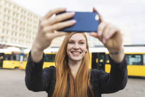 Porträt einer rothaarigen jungen Frau, die ein Selfie mit ihrem Smartphone macht, Berlin, Deutschland, lizenzfreies Stockfoto