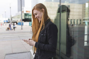 Rothaarige junge Frau, die eine SMS schreibt, Berlin, Deutschland - WPEF02006