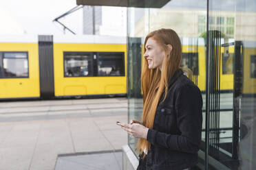 Rothaarige junge Frau mit Smartphone in der Stadt, Berlin, Deutschland - WPEF02007