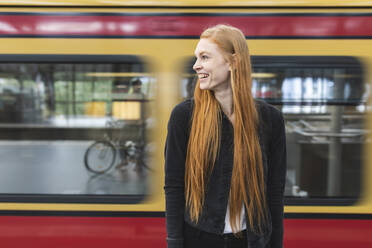 Lachende rothaarige junge Frau, die am Bahnsteig wartet, Berlin, Deutschland - WPEF02012