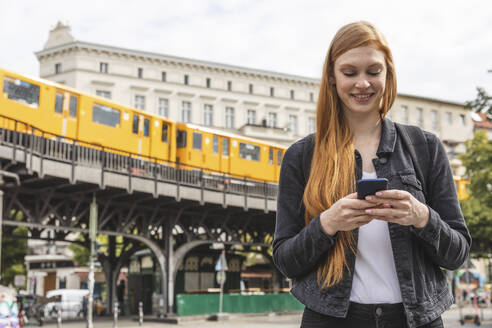 Porträt einer rothaarigen jungen Frau mit Smartphone, Berlin, Deutschland - WPEF02017