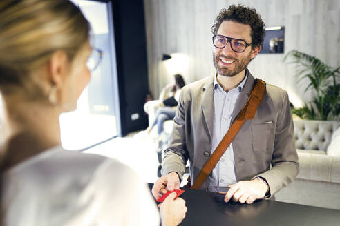 Smiling businessman handing over credit card at reception - JSRF00662