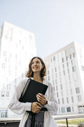 Smiling woman carryiing folder in the city - JRFF03757