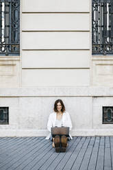 Businesswoman sitting on ground in the city, using laptop - JRFF03765