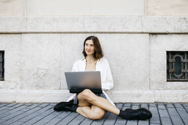 Geschäftsfrau, die in der Stadt auf dem Boden sitzt und einen Laptop benutzt - JRFF03768