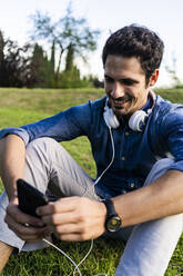 Smiling man sitting on a meadow using his smartphone - GIOF07171