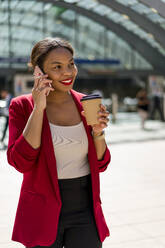 Porträt einer lächelnden Geschäftsfrau mit Kaffee zum Mitnehmen am Telefon, London, UK - MAUF02939