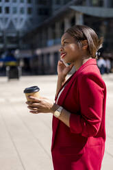 Lächelnde Geschäftsfrau mit Kaffee zum Mitnehmen am Telefon, London, UK - MAUF02940