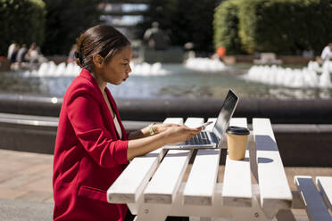 Geschäftsfrau arbeitet im Freien an einem Laptop, London, UK - MAUF02949