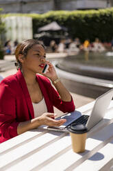 Businesswoman on the phone with laptop and coffee to go outdoors, London, UK - MAUF02950