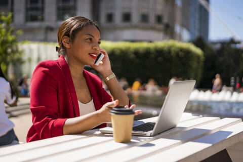 Businesswoman on the phone with laptop and coffee to go outdoors, London, UK stock photo