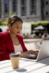Porträt einer lächelnden Geschäftsfrau, die im Freien an einem Laptop arbeitet, London, UK - MAUF02953