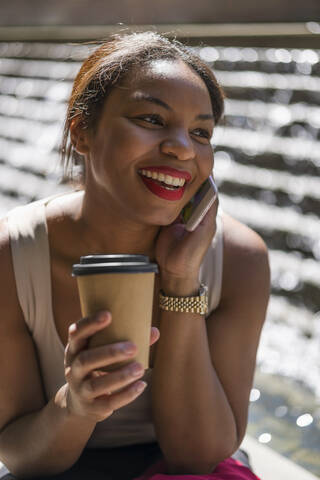 Porträt einer glücklichen Frau mit Kaffee zum Mitnehmen am Telefon, London, UK, lizenzfreies Stockfoto