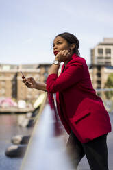 Porträt einer nachdenklichen Geschäftsfrau, die sich an ein Brückengeländer lehnt und nach oben schaut, London, UK - MAUF02961