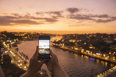 Woman's hands holding smartphone with a photo of panoramic view of Porto at sunset, Portugal - AHSF00871