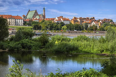 Poland, Masovian Voivodeship, Warsaw, Overgrown riverbank of Vistula river with skyline of Warsaw Old Town in background - ABOF00443