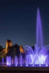 Polen, Woiwodschaft Masowien, Warschau, Lila Brunnen im Multimedia Fountain Park bei Nacht mit der St. Marys Kirche im Hintergrund - ABOF00449