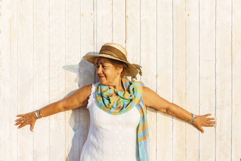 Portrait of a senior woman with outstetched arms at a wooden wall - MOSF00007