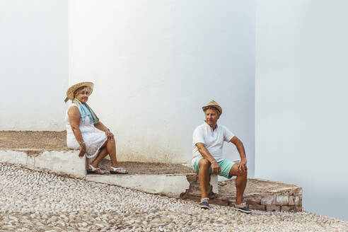 Senior tourist couple sitting on steps in a village, El Roc de Sant Gaieta, Spain - MOSF00021