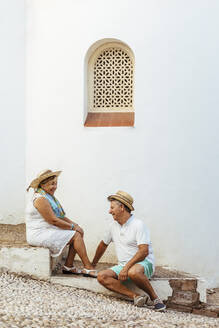 Happy senior tourist couple sitting on steps in a village, El Roc de Sant Gaieta, Spain - MOSF00022