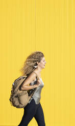 Junge Frau trägt Rucksack vor gelbem Hintergrund - DAMF00141