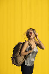 Porträt einer jungen Frau mit Rucksack vor einem gelben Hintergrund - DAMF00142
