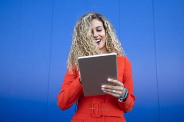 Porträt einer jungen Frau in einem roten Kleid vor einem blauen Hintergrund mit einem digitalen Tablet - DAMF00155