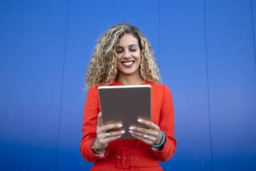 Porträt einer jungen Frau in einem roten Kleid vor einem blauen Hintergrund mit einem digitalen Tablet - DAMF00156