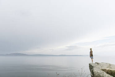 Frau steht auf einem Felsen und blickt auf das Meer - AHSF00872