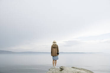 Frau mit Kamera auf einem Felsen stehend, Blick auf das Meer, Rückansicht - AHSF00873