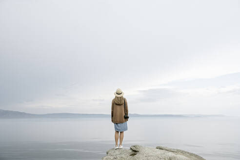 Frau mit Kamera auf einem Felsen stehend, Blick auf das Meer, Rückansicht - AHSF00873