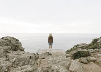 Frau mit Kamera auf einem Felsen stehend, Blick auf das Meer, Rückansicht - AHSF00874