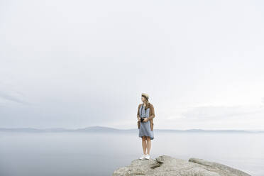 Frau mit Kamera auf einem Felsen stehend, mit Blick auf das Meer - AHSF00878