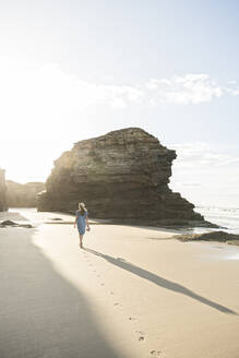 Woman walking on beach with rocks, rear view - AHSF00890