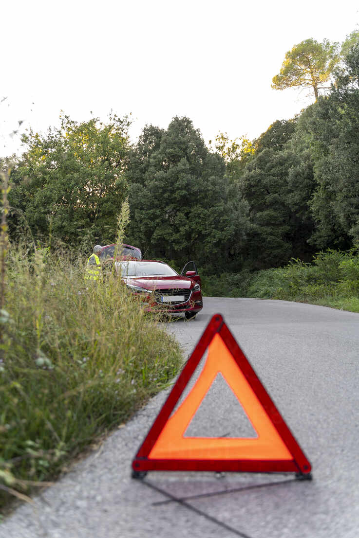 Warndreieck vor einem kaputten Auto auf einer Landstraße, lizenzfreies  Stockfoto