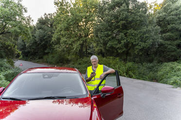 Ein älterer Mann steht an seinem kaputten Auto und benutzt sein Smartphone - AFVF04051