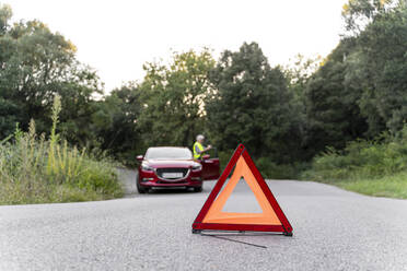 Warning triangle in front of a senior man's broken car on a country road - AFVF04053